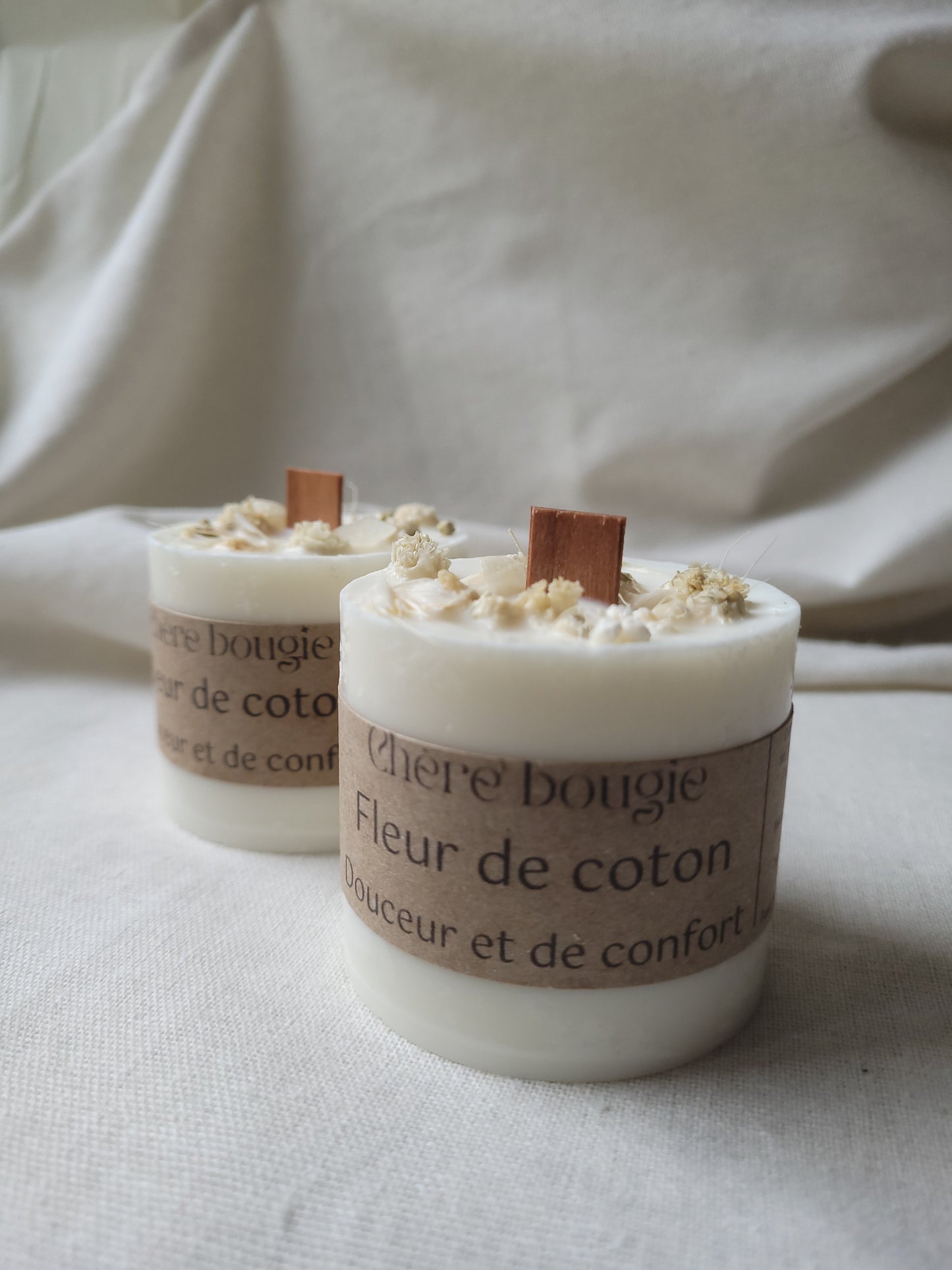 Bougie artisanale fleur de coton dans un élégant contenant noir, mise en scène sur une table décorative.